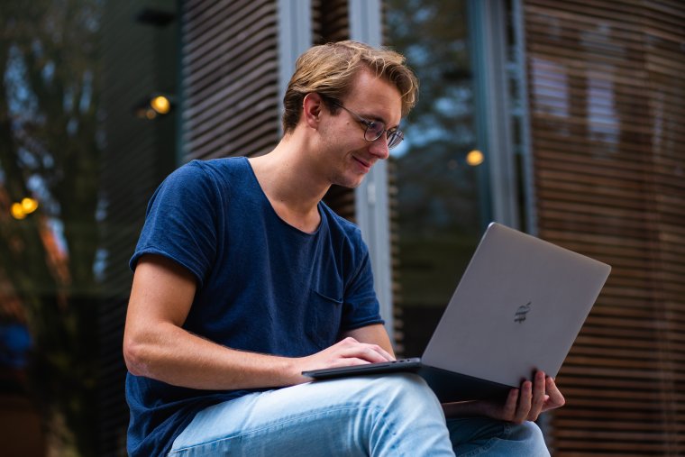 Ung mann studerer på laptop utendørs.