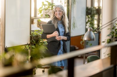 Kvinne med laptop står i et grønt og lyst kontorlandskap.