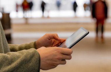 Person holder en mobiltelefon, uskarpe mennesker i bakgrunnen.