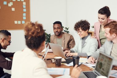 Fire personer diskuterer rundt et bord med bærbare datamaskiner og notater.