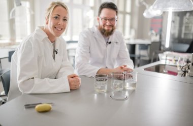 To personer i labfrakker med kjemikalier på et laboratoriebord.